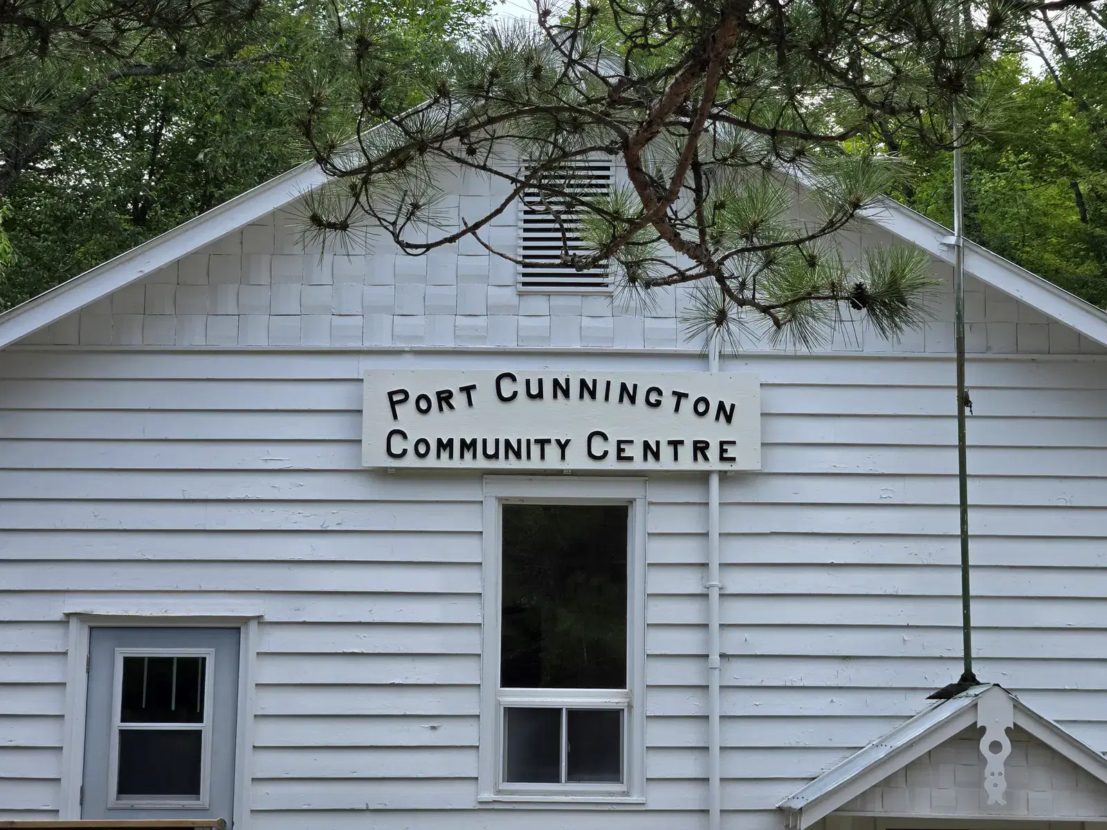 The hall's hand-lettered sign mounted below the shingled gable, framed by a white pine branch.